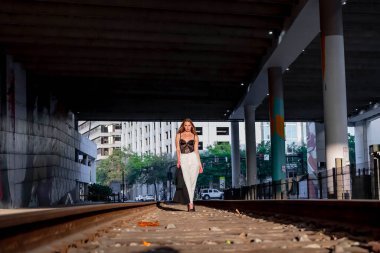 Sarışın bir model gün batımında tren raylarında poz veriyor.