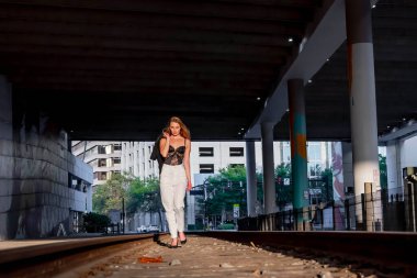 Sarışın bir model gün batımında tren raylarında poz veriyor.