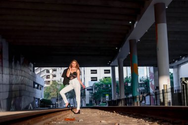 Sarışın bir model gün batımında tren raylarında poz veriyor.