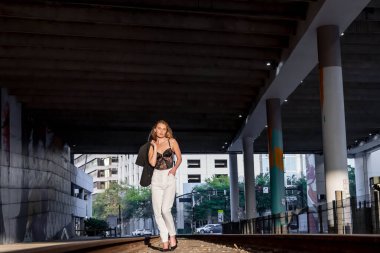 Sarışın bir model gün batımında tren raylarında poz veriyor.