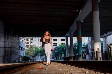 Sarışın bir model gün batımında tren raylarında poz veriyor.