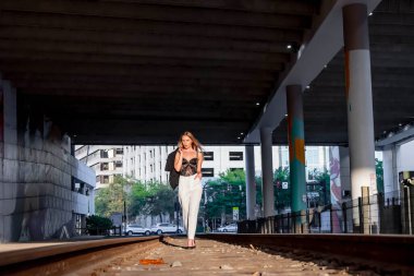 Sarışın bir model gün batımında tren raylarında poz veriyor.