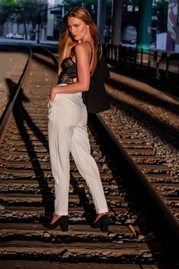 Sarışın bir model gün batımında tren raylarında poz veriyor.