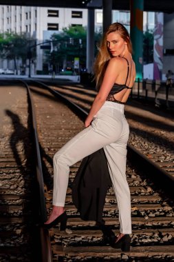 Sarışın bir model gün batımında tren raylarında poz veriyor.