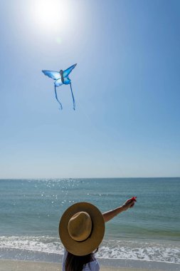 Güzel, olgun bir esmer model sahilde uçurtmasını uçururken günün tadını çıkarıyor.
