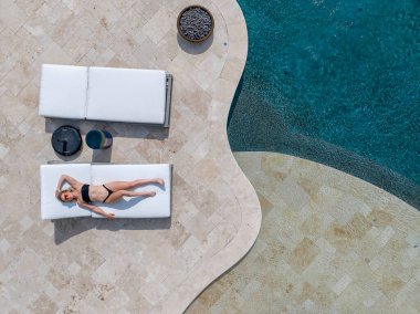 A gorgeous blonde bikini model enjoys a day off at home lounging by the swimming pool