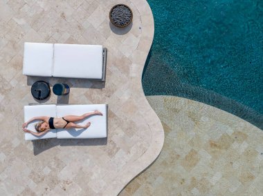 A gorgeous blonde bikini model enjoys a day off at home lounging by the swimming pool