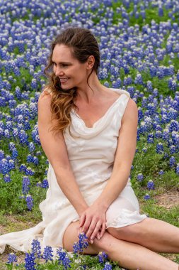Güzel bir esmer model, bir bahar günü mavi boneli çiçeklerle dolu bir tarladan zevk alır.