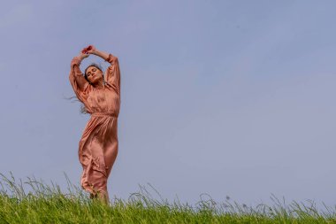 Güzel bir esmer model, rüzgarlı bir bahar gününde çayırda poz verir.