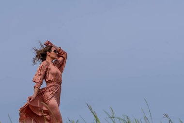 Güzel bir esmer model, rüzgarlı bir bahar gününde çayırda poz verir.