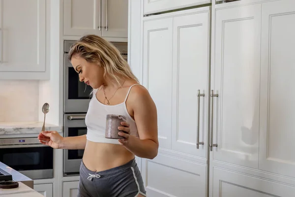 Stock image A beautiful young blonde female enjoys a snack in a white kitchen at home