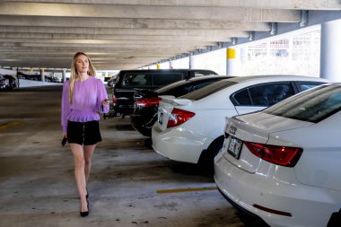 Muhteşem sarışın bir model başarılı bir toplantıdan sonra kapalı otoparkta arabasına doğru yürür.