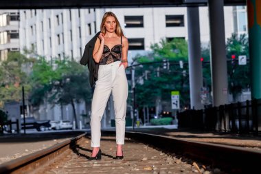 Sarışın bir model gün batımında tren raylarında poz veriyor.