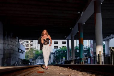 Sarışın bir model gün batımında tren raylarında poz veriyor.