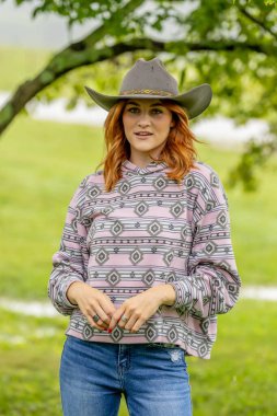 Güzel bir kızıl saçlı model, kovboy kız kıyafeti giyerek bir ülkede poz veriyor..