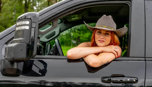 美しい赤毛モデルは彼女の農場でカウボーイの帽子をかぶっている間彼女のトラックに座っています — ストック写真