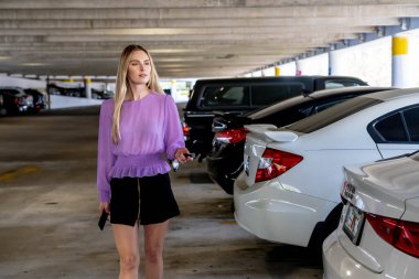 Muhteşem sarışın bir model başarılı bir toplantıdan sonra kapalı otoparkta arabasına doğru yürür.