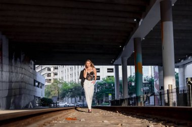 Sarışın bir model gün batımında tren raylarında poz veriyor.