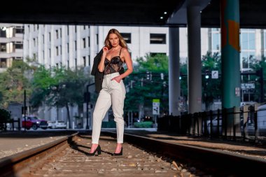 Sarışın bir model gün batımında tren raylarında poz veriyor.