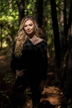 Muhteşem sarışın bir model, kasvetli bir orman ortamında poz veriyor.