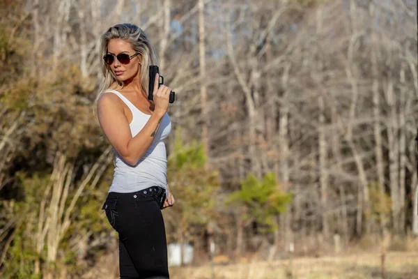 stock image A beautiful blonde model holds a pistol for protection on a sunny day.