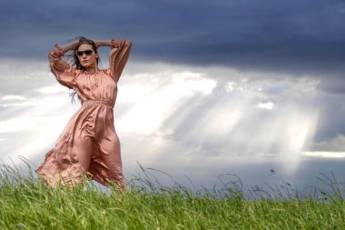 Güzel bir esmer model, rüzgarlı bir bahar gününde çayırda poz verir.