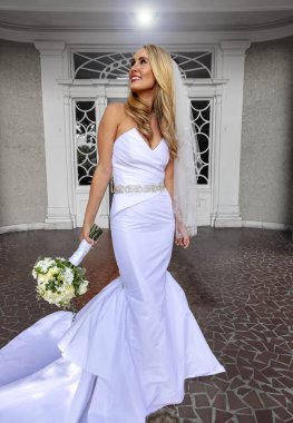 Gelinlik içindeki parlak sarışın gelin, düğün öncesi fotoğraflar için zarifçe poz veriyor, özel gününün heyecanını ve güzelliğini yakalıyor..