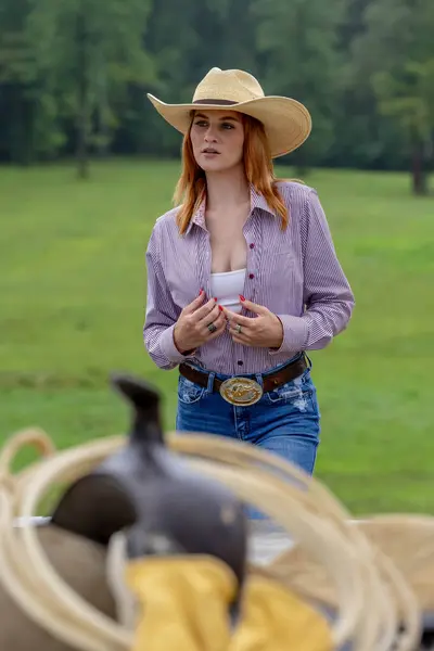 A beautiful redhead model poses in a country setting wearing cowgirl attire.
