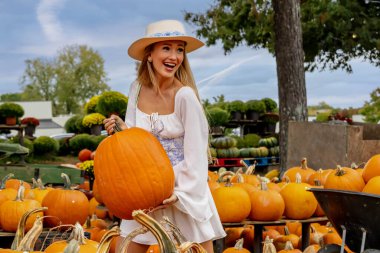 Güzel bir Avrupalı sarışın kadın yaklaşan sonbahar festivalleri için balkabağı ve çiçek fotoğrafı çekiyor.