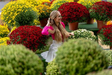 Güzel bir Avrupalı sarışın kadın, önümüzdeki sonbahar festivalleri için bazı çiçeklerin fotoğrafını çekiyor.