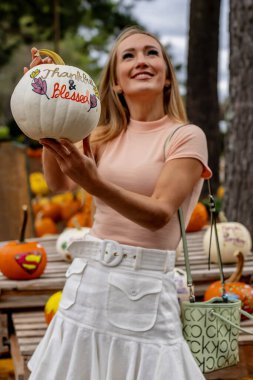Güzel bir Avrupalı sarışın kadın yaklaşan sonbahar festivalleri için balkabağı ve çiçek fotoğrafı çekiyor.