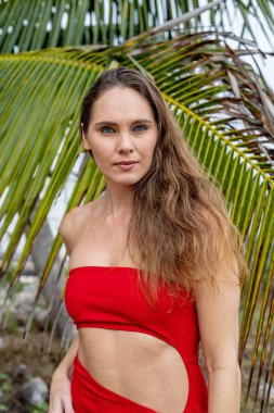 Göz kamaştırıcı esmer, canlı kırmızı bir elbise içinde ışıl ışıl, Karayip kıyılarını zarafetle süslüyor, tropik cennetin ortasında güzelliği somutlaştırıyor.