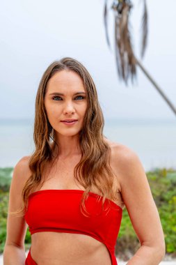 Göz kamaştırıcı esmer, canlı kırmızı bir elbise içinde ışıl ışıl, Karayip kıyılarını zarafetle süslüyor, tropik cennetin ortasında güzelliği somutlaştırıyor.