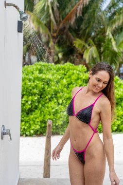 Sahildeki şelalenin altında bikinili güzellik yağmurları, Karayipler 'in güneşli dinginliğine dalmış bir cazibe ve rahatlama görüntüsü.