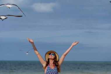 Çekici bir kadın, turkuaz sular ve altın kumlarla çevrili Karayipler sahilindeki martıları zarifetle besler ve güzel bir tatil sahnesi yaratır.