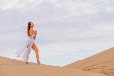 Zarif model kum tepelerindeki doğanın güzelliğini kucaklıyor, engin, doğal ihtişamın arkaplanına karşı zarafeti simgeliyor.