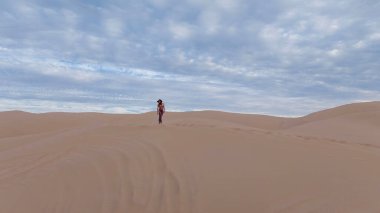 Zarif model kum tepelerindeki doğanın güzelliğini kucaklıyor, engin, doğal ihtişamın arkaplanına karşı zarafeti simgeliyor.