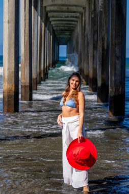 Nefes kesen kadın kumsaldaki mutluluğun tadını çıkarıyor, bir rıhtımın yanında, açık mavi gökyüzünün altında, deniz kıyısında mükemmel bir günün dinginliğini kucaklıyor.