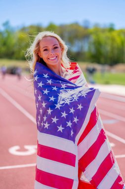Gururlu Amerikan sporcusu Amerikan bayrağını sallıyor. Başarılı bir yerel yarışın ardından ülkesini onurlandırıyor. Vatanseverlik ve saygıyı simgeliyor..