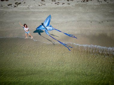 Güzel, olgun bir esmer model sahilde uçurtmasını uçururken günün tadını çıkarıyor.