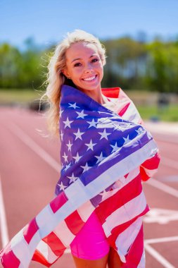 Gururlu Amerikan sporcusu Amerikan bayrağını sallıyor. Başarılı bir yerel yarışın ardından ülkesini onurlandırıyor. Vatanseverlik ve saygıyı simgeliyor..