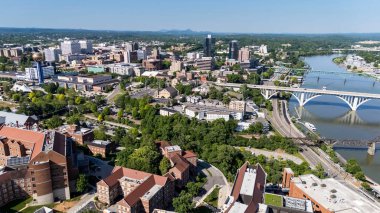 An aerial view of Knoxville, Tennessee reveals a vibrant cityscape with a mix of historic and modern buildings, the Tennessee River weaving through downtown, lush green parks, and the distant Smoky Mountains framing the horizon. clipart