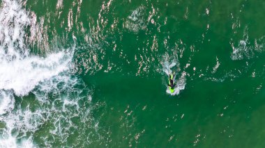 Sörfçü, Kaliforniya 'nın berrak ve ılık yaz gökyüzü altında, altın güneş ışığı ve masmavi sularla çevrelenmiş, nefes kesici bir hava manzarası içinde dalgaları yakalar..