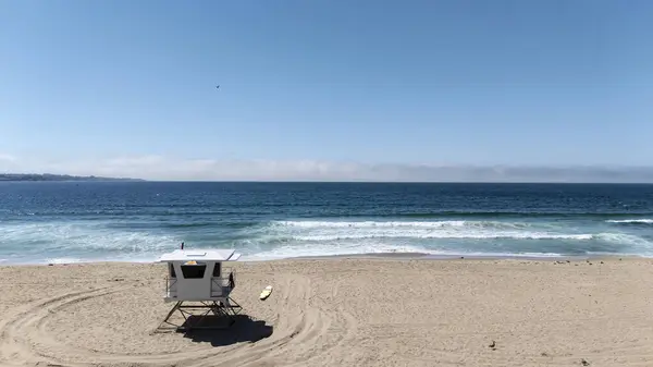 stock image A lifeguard station stands sentinel over a stunning California beach, bathed in warm sunshine and embraced by azure waves, in a serene aerial view.