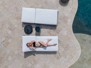 A gorgeous blonde bikini model enjoys a day off at home lounging by the swimming pool