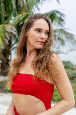 Göz kamaştırıcı esmer, canlı kırmızı bir elbise içinde ışıl ışıl, Karayip kıyılarını zarafetle süslüyor, tropik cennetin ortasında güzelliği somutlaştırıyor.