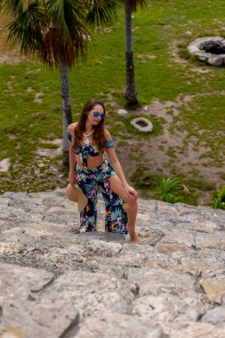 A radiant young woman explores the Xcambo Mayan ruins, her presence weaving elegance with ancient history, under the Caribbean sun's golden embrace clipart