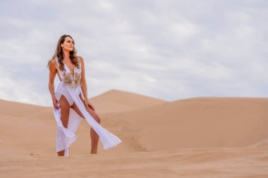 Zarif model kum tepelerindeki doğanın güzelliğini kucaklıyor, engin, doğal ihtişamın arkaplanına karşı zarafeti simgeliyor.