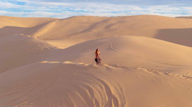 Zarif model kum tepelerindeki doğanın güzelliğini kucaklıyor, engin, doğal ihtişamın arkaplanına karşı zarafeti simgeliyor.
