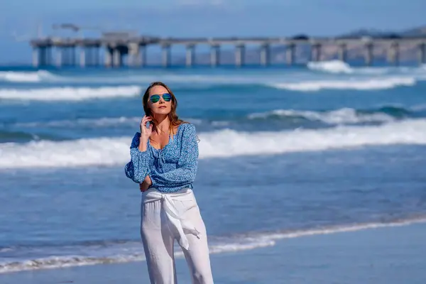 stock image Breathtaking woman basks in beach bliss, near a pier, under clear blue skies, embracing the serenity of a perfect day by the sea